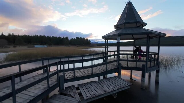 Laguna La Zeta near Esquel, Chubut, Argentina, featuring lakeside pavilion, wooden docks, reed wetlands and Patagonian forest landscape under evening sky, FPV orbit and forward flight shot.
