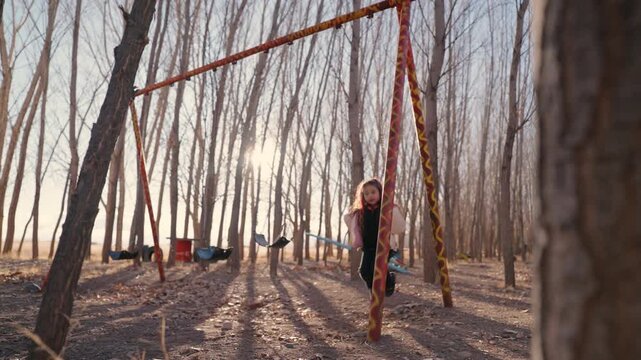 Child having fun on a swing surrounded by tall trees and warm evening light.