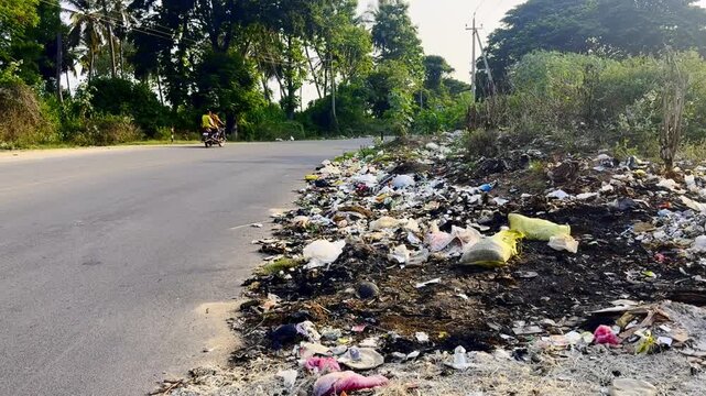Realistic video footage of household and plastic waste dumped carelessly beside a rural village road, highlighting environmental pollution and waste management challenges in rural areas. 
