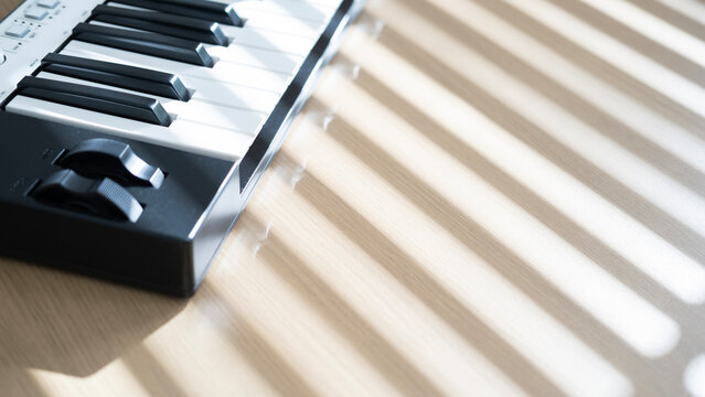 Close up of a midi keyboard on a wooden table with warm morning sunlight and soft window shadows in a cozy home music space.