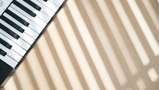 Top view of a midi keyboard on a wooden table with bright morning sunlight and striped shadows creating a calm creative music atmosphere.