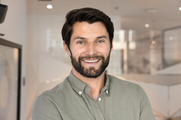 Obraz premium Head shot close up portrait of confident bearded man smiling at camera standing in modern office, representing professionalism, success and leadership in business. Company boss, or CEO profile picture