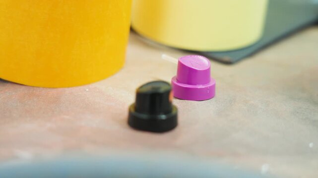 Colorful spray bottle caps and automotive paint accessories on a workshop table in a professional bodyshop environment for vehicle refinishing and industrial repair process, UHD.