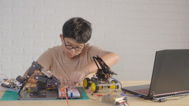 Asian young student building electronic circuits and a robotics project at home with robotic devices and a laptop. Concept of STEM education, engineering skills, and technology learning.