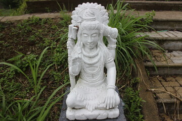 Fototapeta premium White statue of Shiva in meditative pose surrounded by green grass and steps.