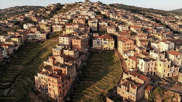 Aerial view dense populated hillside town traditional colorful buildings terraced fields bathed warm golden light vibrant community historic architecture showcasing Madagascar Independence Day