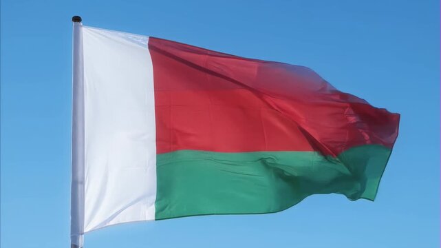Flag of Madagascar proudly waving against clear blue sky, showcasing national colors white, red, and green, a vivid symbol of national sovereignty, unity, and pride for Madagascar Independence Day