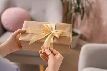 Fototapeta na wymiar Hands untying golden ribbon on brown kraft paper gift box, holiday celebration and special occasion present, the act of unwrapping a gift evokes joy and anticipation