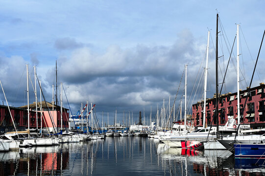 panoramic view of the Genoa Sea Port, harbor and marina. white pleasure yachts, and sail boats in diminishing perspective. old towering historic stone lighthouse. smoot water surface with reflections.