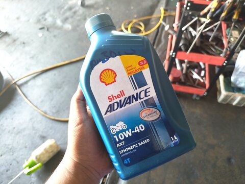 KUALA TERENGGANU MALAYSIA- JUNE 09. 2026. A close-up of a person's hand holding a 1-litre blue plastic bottle of Shell Advance AX7 4T 10W-40 synthetic-based motorcycle engine oil