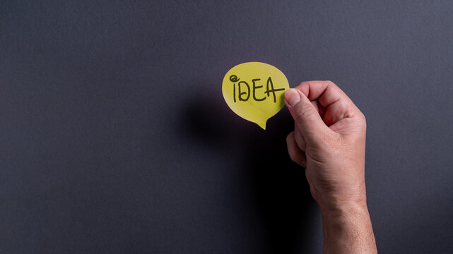 Male hand holding yellow speech bubble with idea text on dark background