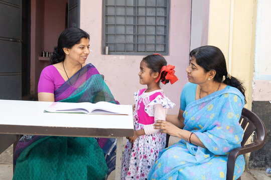 Indian educator and mother sitting with a girl child, childhood learning and development outdoor, educational support in rural india.