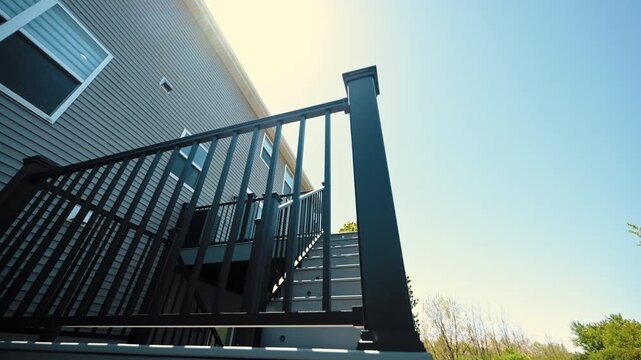 Modern elevated backyard deck attached to house featuring black metal railings, outdoor stairs