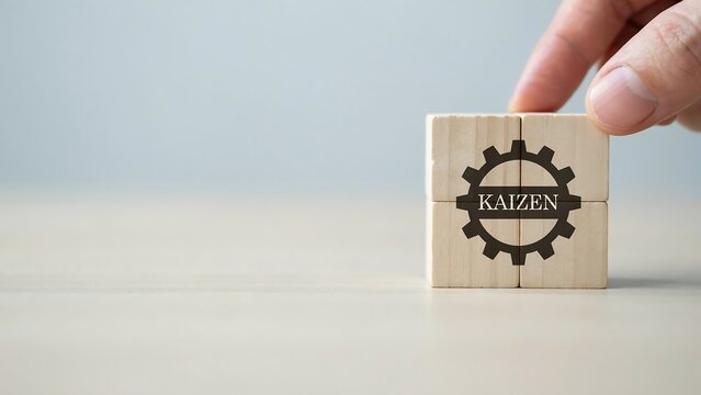 A hand places a wooden block with a Kaizen gear logo on a table indoors