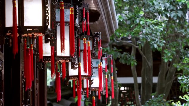 A row of lanterns adorned with red tassels hangs along a traditional corridor surrounded by lush greenery. Perfect for cultural documentaries or heritage travel features.