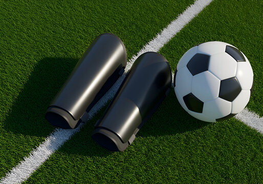 Black shin guards and soccer ball on a grassy field. Athletes' protective equipment resting on the playing surface. Professional soccer player's equipment at a sports field -