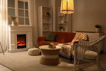 Obraz premium Cozy living room interior with electric fireplace, comfortable sofa, wicker furniture, and warm lighting for relaxation
