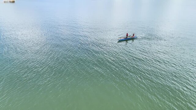 Aerial drone view of a lone fisherman paddles a dugout canoe through the vibrant green waters of Inner Malampaya Sound in Philippines