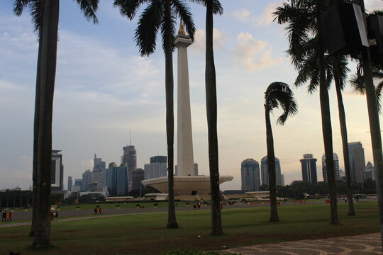 National monument of Indonesia monas standing tall amidst palm trees at sunset.
