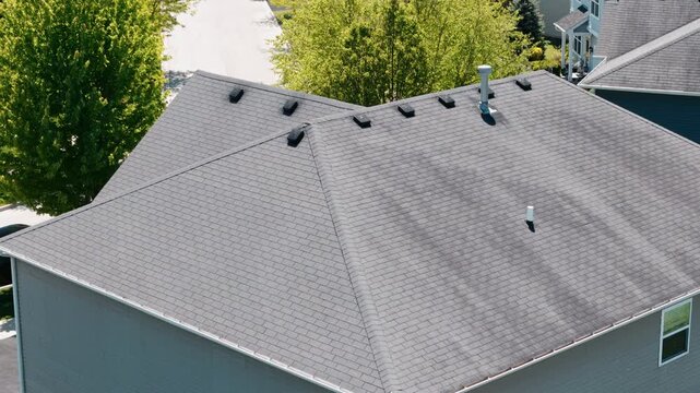 Aerial view of a residential house roof with asphalt shingles, roof vents, and modern roofing construction in a suburban neighborhood.