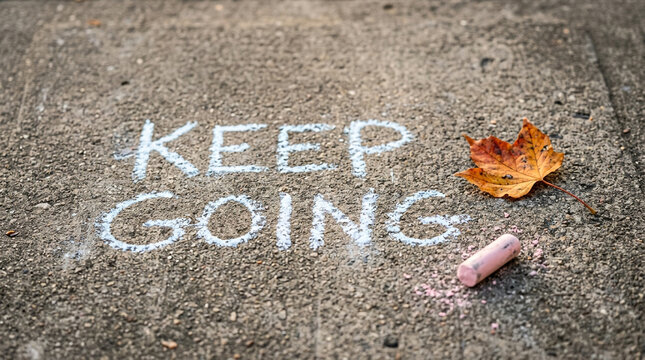 Inspirational Keep Going message written in chalk on asphalt, motivational quote on sidewalk with autumn leaf, perseverance concept on urban pavement