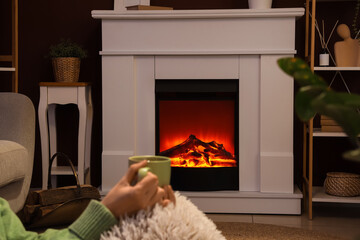 Obraz premium Cozy home interior with person relaxing by electric fireplace, warm ambiance and comfort in living room