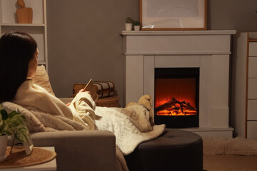 Obraz premium Cozy evening relaxation with woman reading book by electric fireplace, comfortable home atmosphere and leisure activity, peaceful domestic interior with warm lighting and modern furnishings