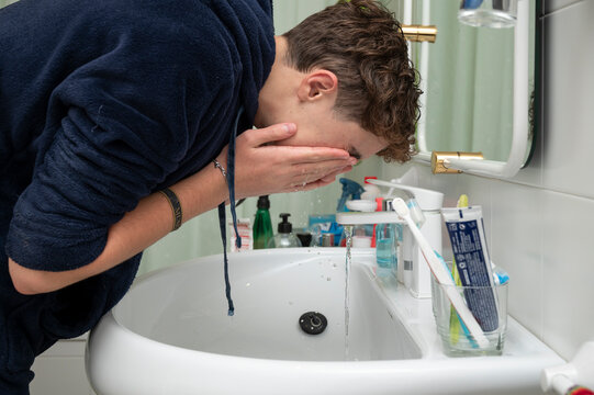 Teenage boy washing his face in the bathroom sink during his morning routine before school at home