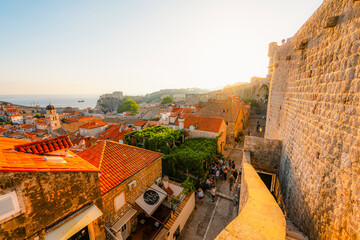 Obraz premium Golden hour panorama of Dubrovnik's historic fortifications and old port at dusk, featuring sunlight on ancient stone walls and Mediterranean architecture in Croatia