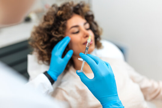 Close up of dermatologist hands in blue gloves holding syringe with face injection filler for patient treatment in aesthetic clinic. Cosmetic dermatology procedure concept with syringe focus.