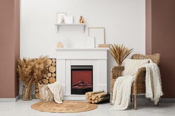 Obraz premium Cozy living room interior with electric fireplace, wicker chair, and pampas grass decor for home comfort