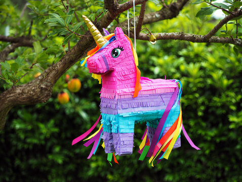 Colorful unicornshaped pinata hanging from a tree branch in a lush green garden setting