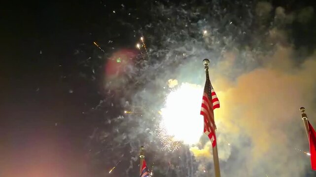 Brilliant fireworks burst in vivid colors above the American flag on a clear night create a dramatic patriotic atmosphere