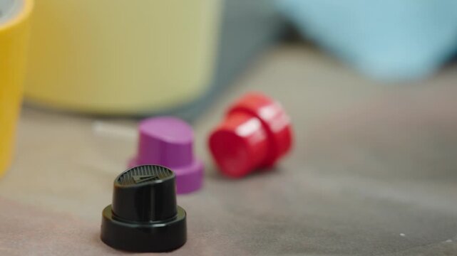 Handheld shot of colorful spray bottle caps and automotive paint accessories on a workshop table in a professional bodyshop environment for vehicle refinishing and industrial repair process, UHD.
