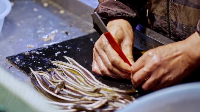 A vendor skillfully prepares eels on a cutting board at a bustling Shanghai market. Ideal for culinary or cultural documentaries.