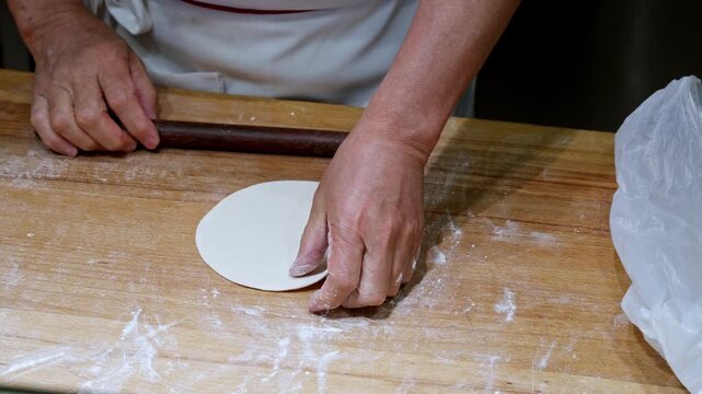 A chef skillfully rolls dough on a wooden surface, preparing dumplings in a traditional Shanghai setting. Ideal for culinary documentaries and cooking tutorials.
