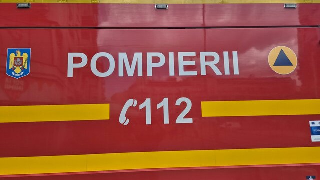 Side panel of a red Romanian fire truck displaying white lettering "POMPIERII", the emergency number "112", yellow stripes, and official emblems. Picture taken on May 31, 2026 in Bucharest.