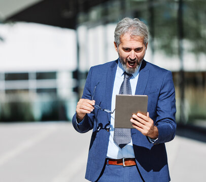 Portrait of a happy smart inteligent senior businessman smiling using a tablet computer standing in the front of the office building