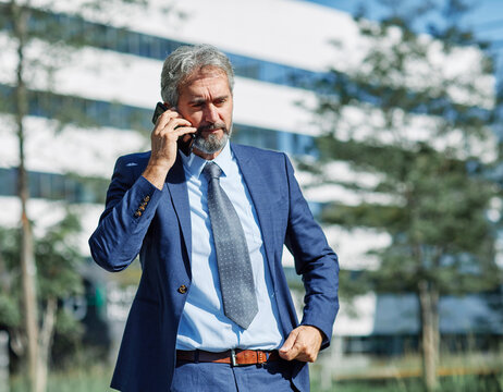 Portrait of a happy smart inteligent senior businessman smiling using a phone smartphone standing in the front of the office building
