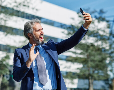 Portrait of a happy smart inteligent senior businessman smiling using a phone smartphone standing in the front of the office building
