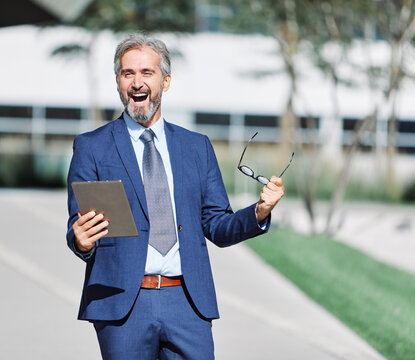 Portrait of a happy smart inteligent senior businessman smiling using a tablet computer standing in the front of the office building