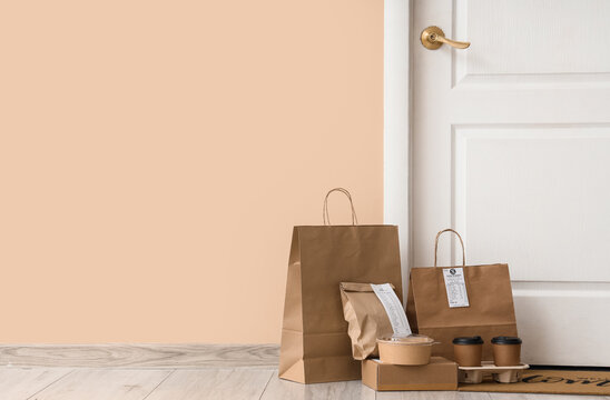 Contactless food delivery service with brown paper bags and coffee cups at front door, home meal takeout