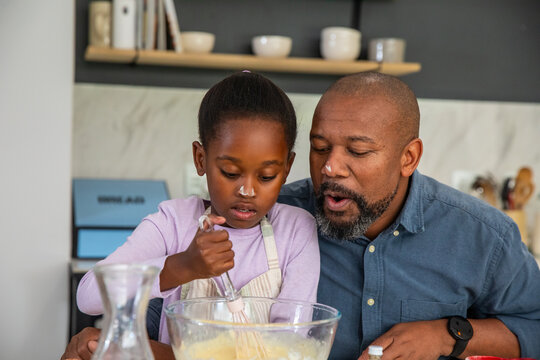 African American father and daughter mixing batter in kitchen with glass bowl and striped apron