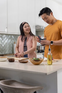 Diverse couple chopping and seasoning food at kitchen island with cutting board, olive oil bottle