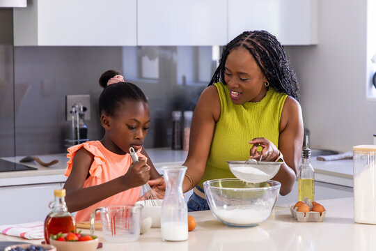 African American mother and child sifting flour at kitchen island with sifter and mixing bowl