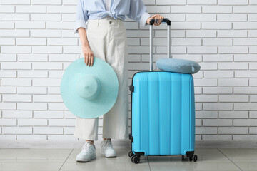 Woman with blue suitcase and sun hat ready for summer vacation travel against white brick wall, the travel essentials suggest a journey or holiday, emphasizing themes of tourism and adventure © Pixel-Shot