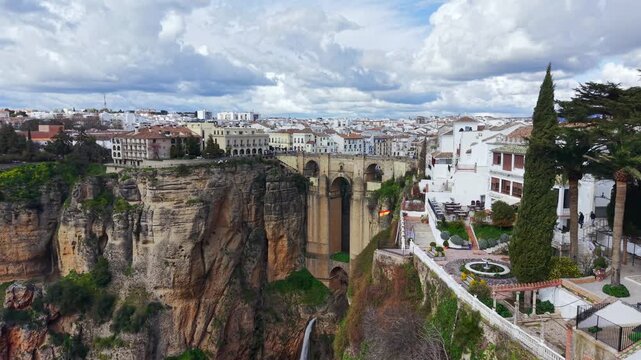 Aerial view flying forward to the historic Puente Nuevo bridge in Ronda, Andalusia, Spain. Drone shot flying in from wide landscape to close-up of the iconic bridge spanning the canyon between cliffs.