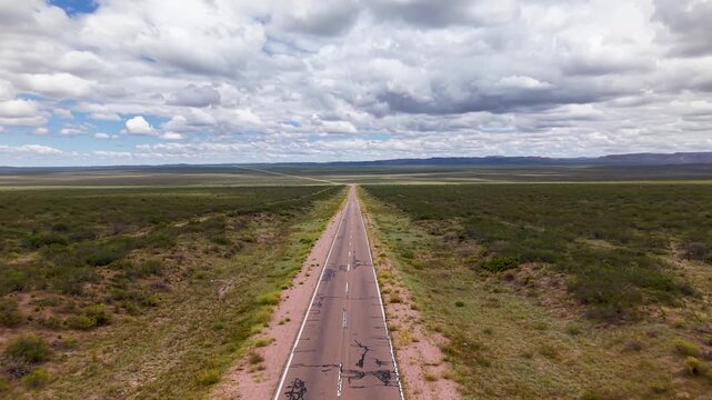 Ruta atravesando paisaje &aacute;rido con vegetaci&oacute;n nativa, autos circulando y nubes en un d&iacute;a soleado
