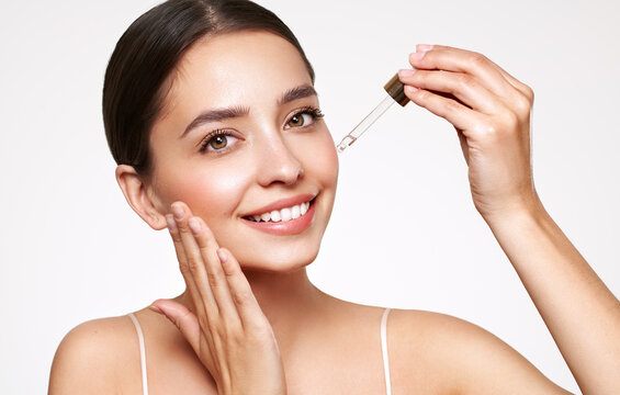 Young beautiful woman applying face serum with pipette. Cosmetic procedures for facial skin care