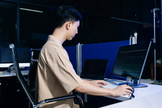 Closeup of a software developer typing data lines on a white keyboard with a monitor showing code setup.